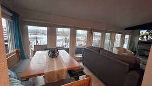 A living room with a wooden table, a sofa, and a television. - Lake-Level Retreat w Hot Tub, Picture Windows & 65” TV for Ultimate Relaxation (Monticello)