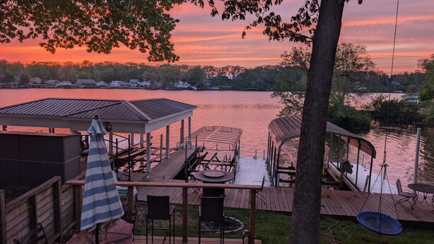 A lakeside deck with a covered seating area, a small pavilion, and a swing chair. - Lake-Level Retreat w Hot Tub, Picture Windows & 65” TV for Ultimate Relaxation (Monticello)