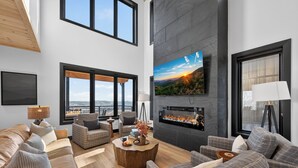 Ein modernes Wohnzimmer mit großem Fernseher, Kamin und bequemen Sitzgelegenheiten.
