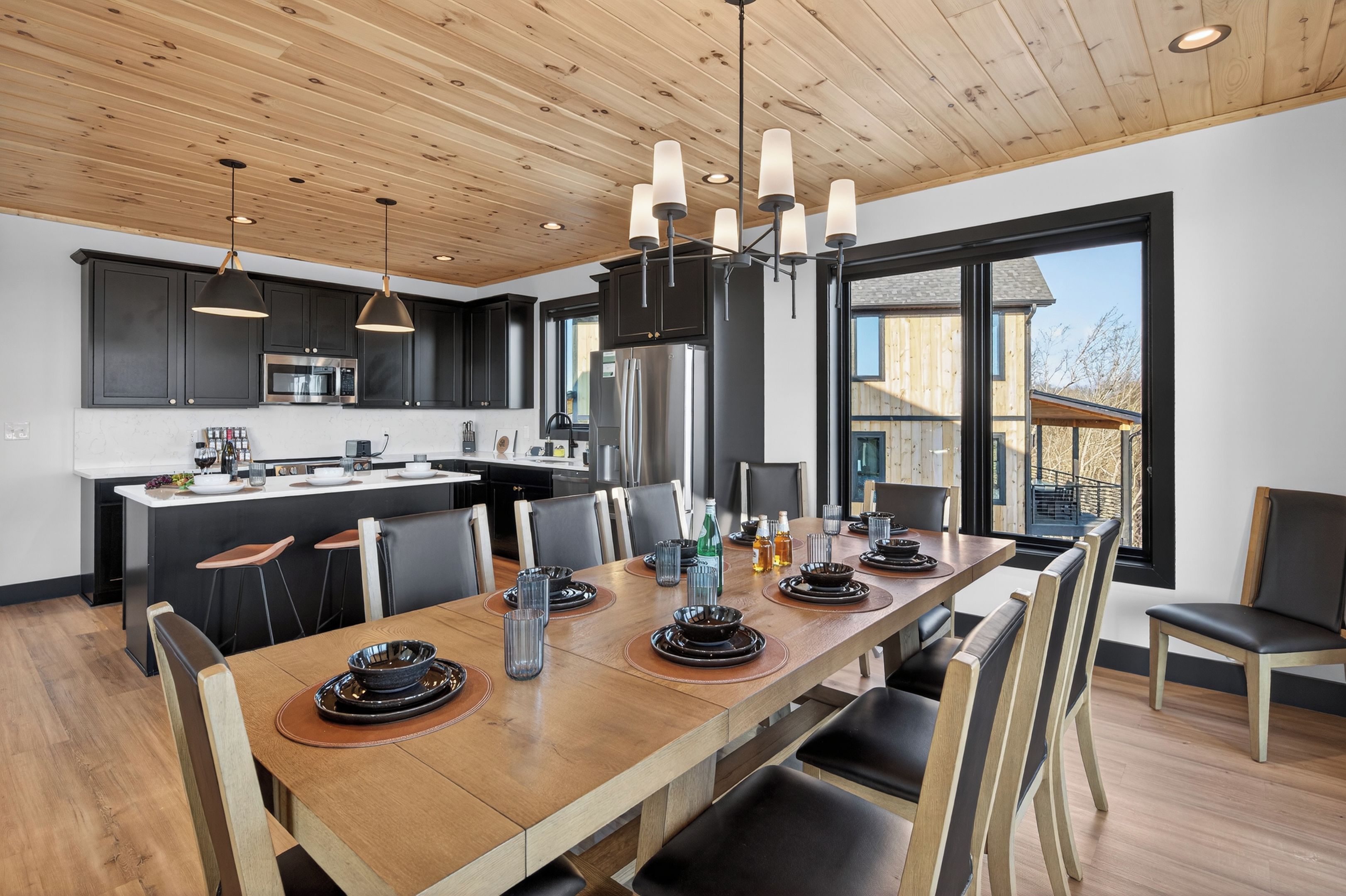 A modern kitchen with dark cabinets, stainless steel appliances, and a wooden dining table set for six.