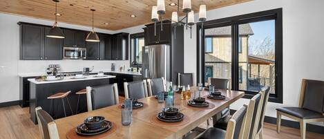 A modern kitchen with dark cabinets, stainless steel appliances, and a wooden dining table set for six.