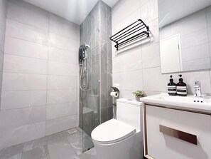 Ein modernes Badezimmer mit Duschkabine aus Glas, einer weißen Toilette, einem Waschbecken mit zwei Shampooflaschen und einem Spiegel darüber.