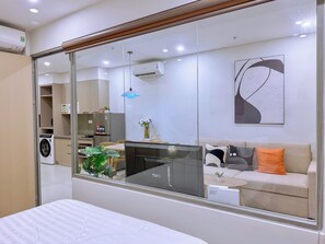 A modern hotel room with a large mirror, a bed, a sofa, a small table, and a washing machine. - The Song Luxury Apartment-Livi Homestay (Ho Chi Minh City)