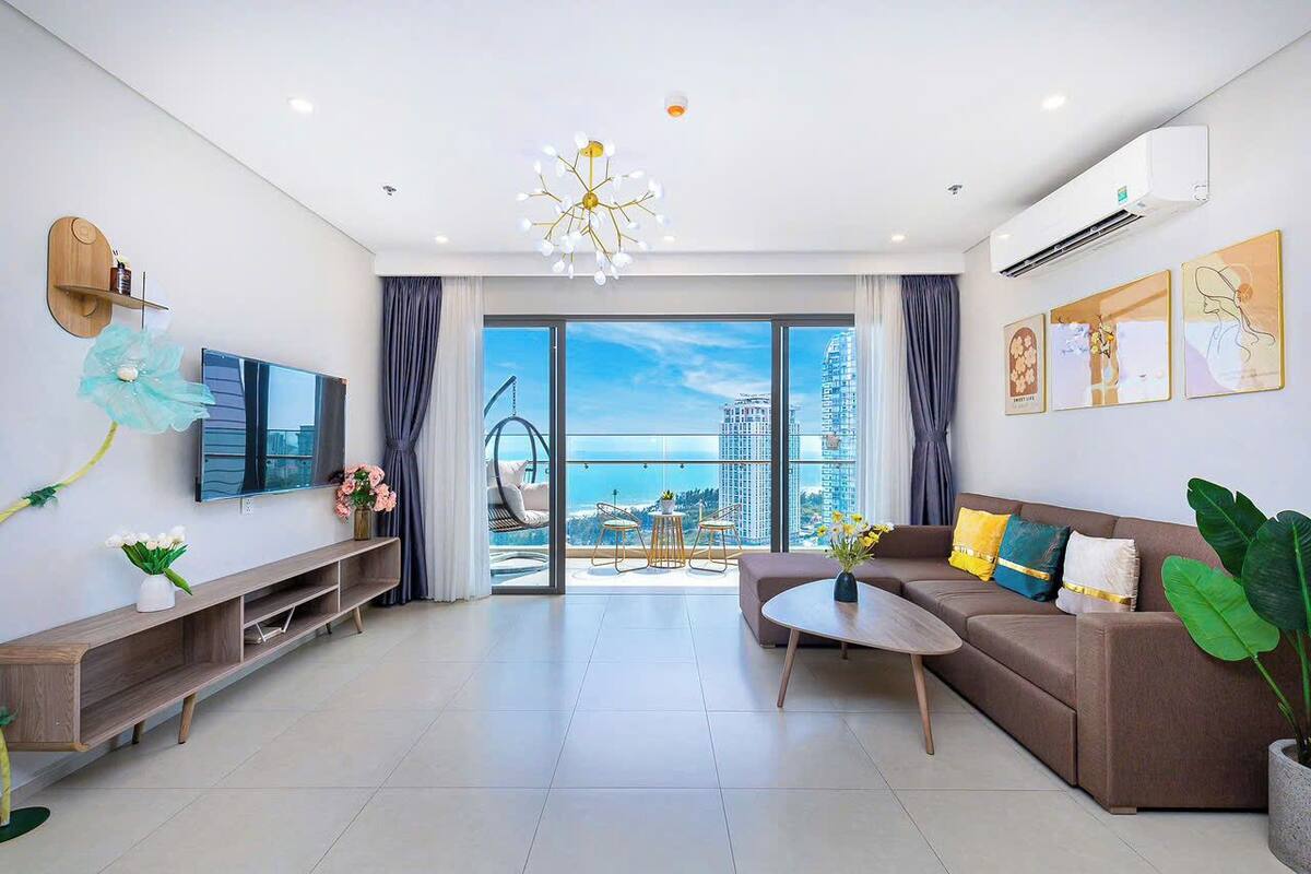 A modern living room with a sofa, coffee table, TV, and a balcony with a city view.