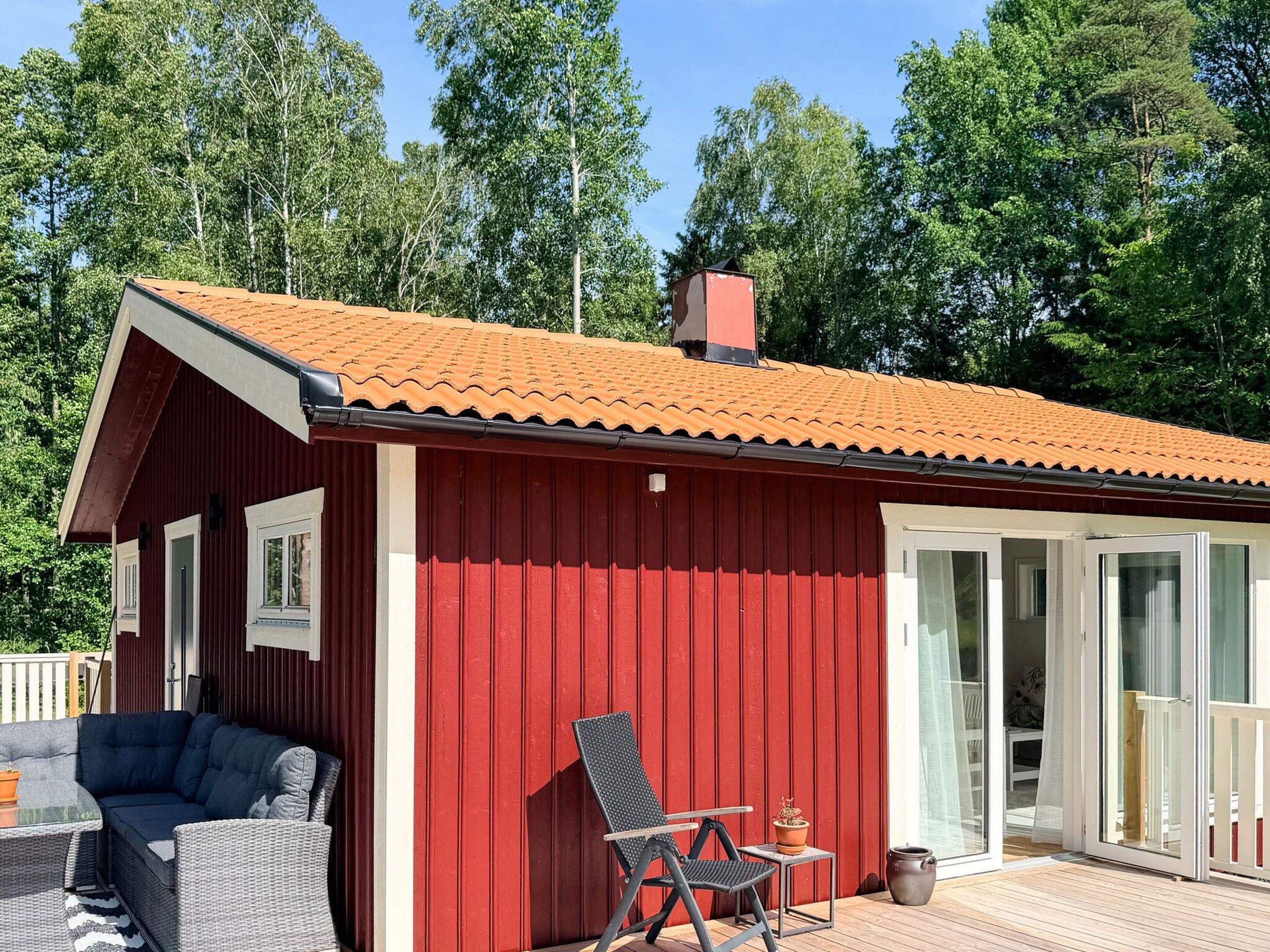 Een rood gebouw met een pannendak, een overdekte patio met meubels en een deur die naar de binnenruimte leidt.