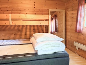 Ein Holzhütten-Zimmer mit Etagenbett, einem Fenster mit Vorhängen und einem Wandheizkörper.