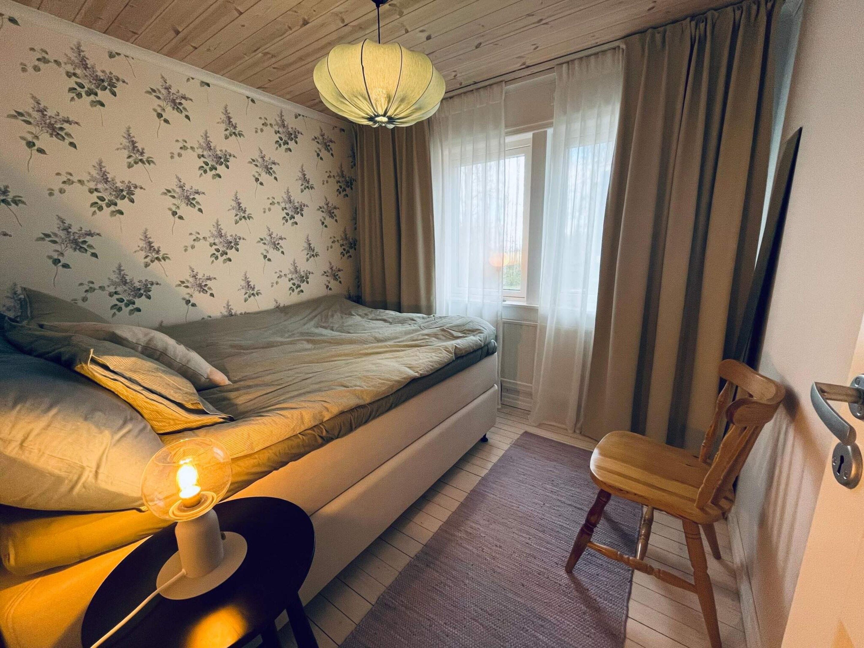 A bedroom with a bed, a chair, a lamp, and a window with curtains.