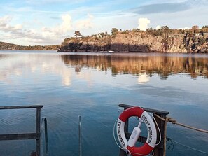 Tyyni järvi, jonka rannalla on kivikkoista maastoa ja laiturissa pelastusrengas.
