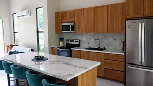 Een moderne keuken met houten kastjes, een roestvrijstalen koelkast, een marmeren aanrechtblad en blauwgroene barstoelen.