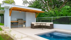 Een modern buitenzwembad met een ingebouwde barbecue en zitplaatsen.