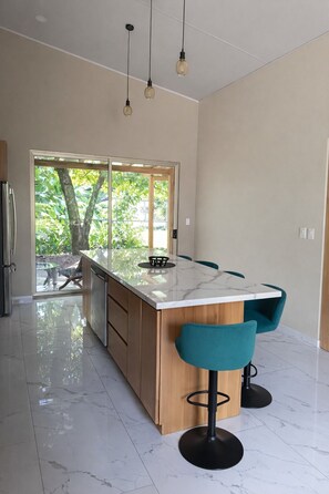 Una cocina moderna con encimera de mármol, armarios de madera y taburetes de bar color turquesa.