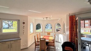 Un comedor con mesa y sillas, una cocina con armarios, y ventanas grandes con arcos.