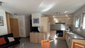 Un espacio habitable compacto con kitchenette, zona de comedor y sala de estar con sofá y televisor.