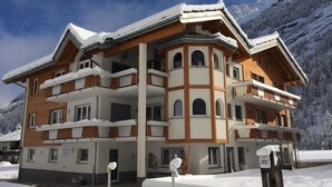 Un edificio de varios pisos con techo nevado y balcones, rodeado de un paisaje montañoso.