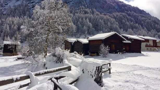 Un paisaje montañoso nevado con cabañas de madera y un banco al frente.