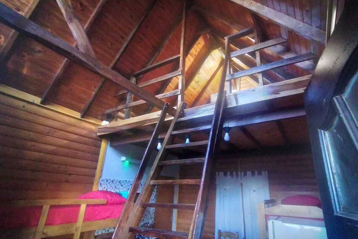 A wooden interior with a ladder, a bed with red bedding, and a white cabinet.