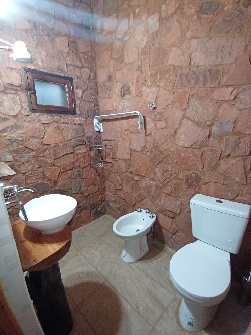 A bathroom with a stone wall, a wooden sink, a bidet, and a toilet.