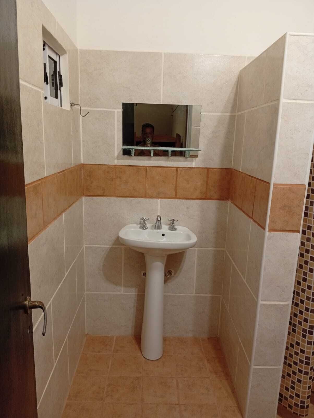 A bathroom with a pedestal sink, a mirror above it, and tiled walls.