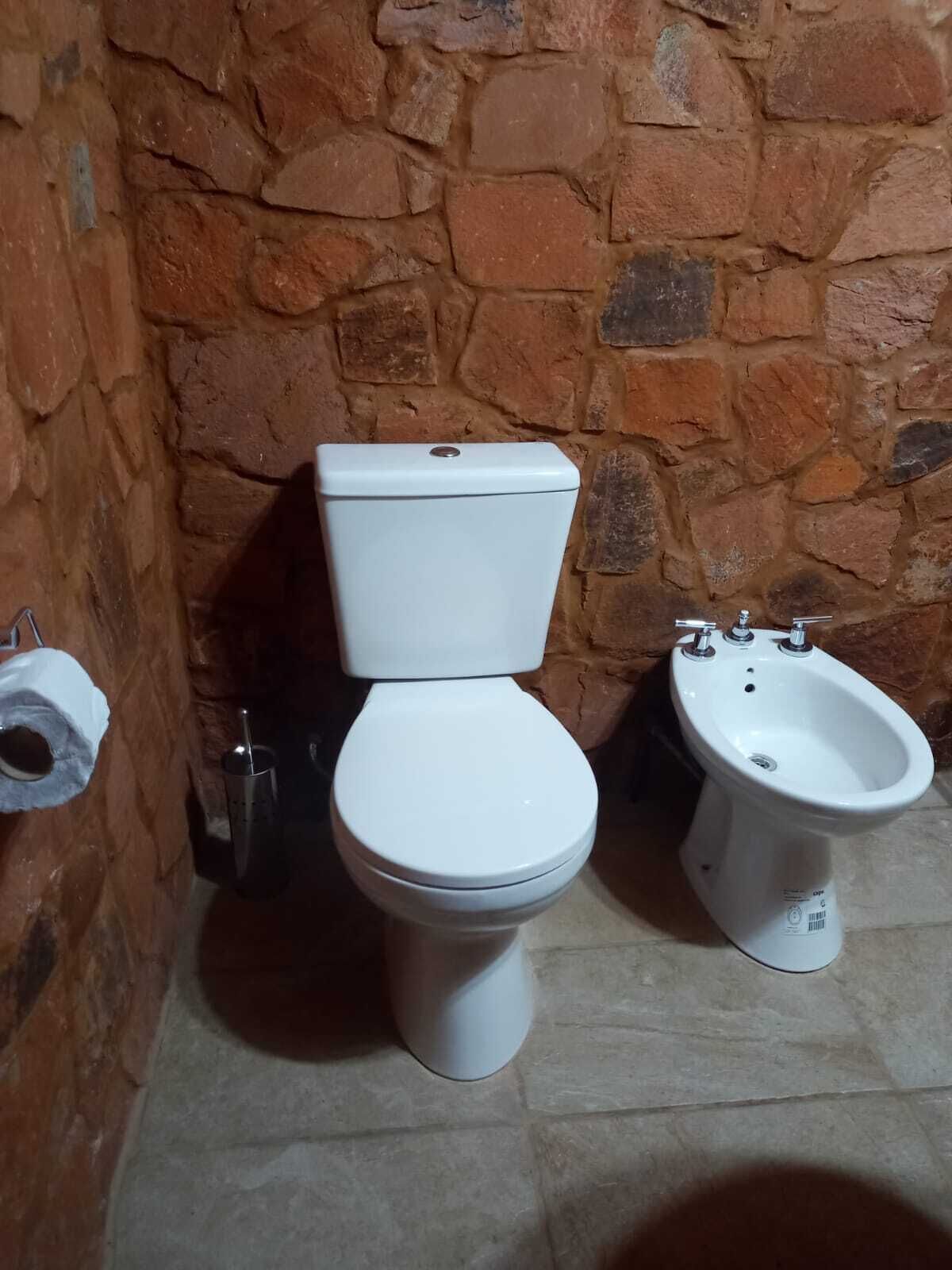 A bathroom with a toilet, bidet, and a stone wall.