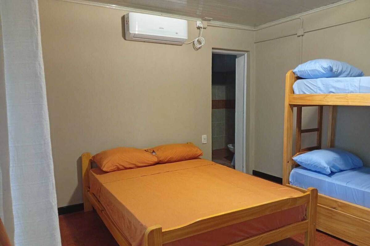 A single bed with an orange bedspread and two pillows, a bunk bed with blue bedding, and a wall-mounted air conditioning unit.