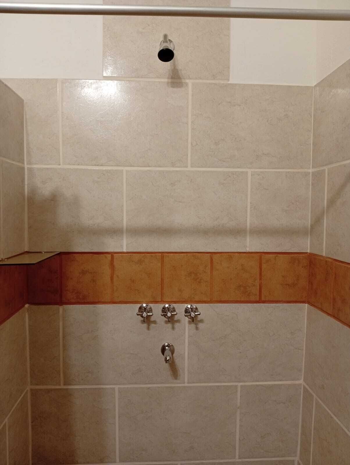 Ducha con azulejos color crema, un borde decorativo marrón y tres elementos metálicos cromados.