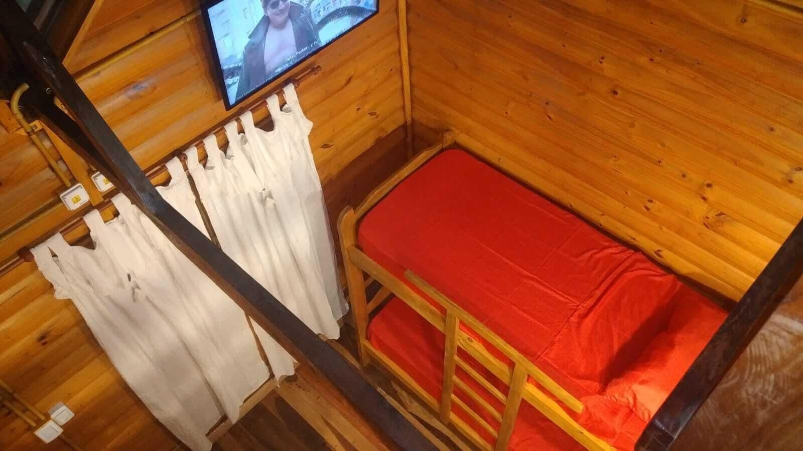 Une pièce de cabane en bois avec un lit superposé, un téléviseur fixé au mur et un rideau.