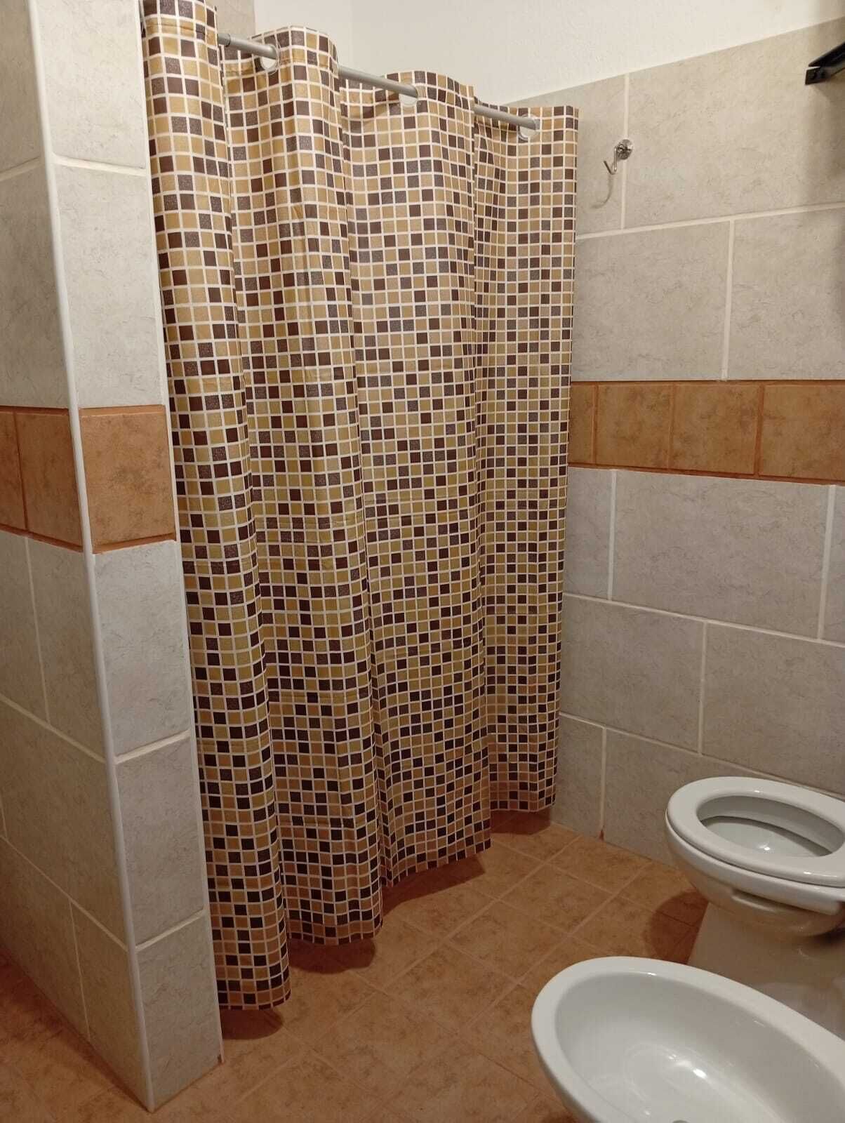 A bathroom with a tiled shower curtain, a toilet, and a urinal.