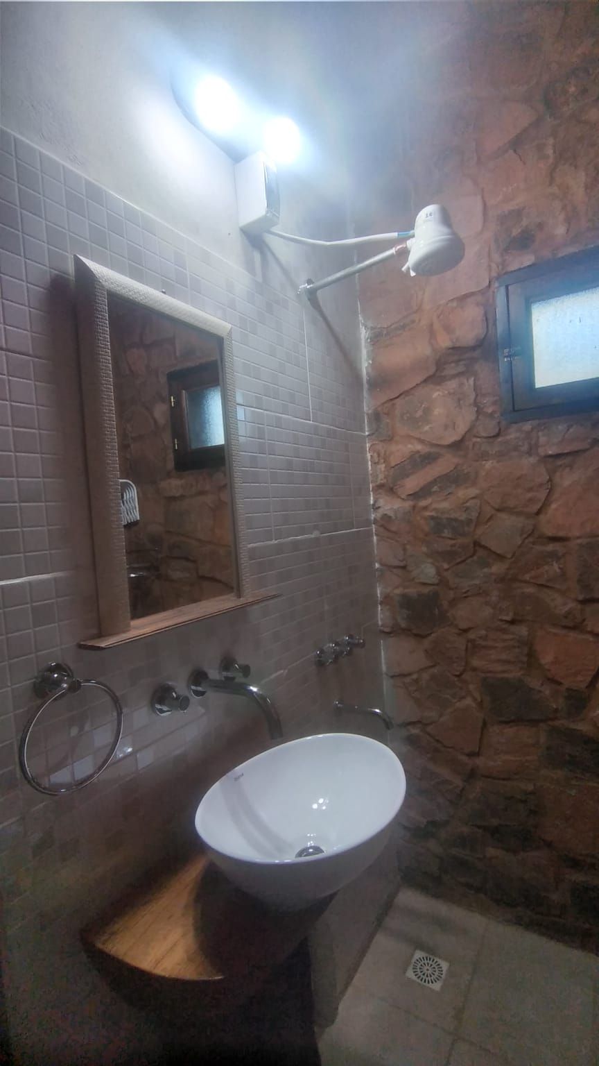A bathroom with a stone wall, a white sink, a mirror, and a shower with a handheld showerhead.