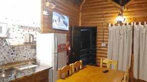 A wooden cabin interior with a kitchen area, a dining table, and a television mounted on the wall. - Cabañas Misioneras  (San Ignacio)