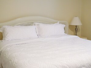 A neatly made bed with white bedding and pillows, a white headboard, and a bedside lamp. - Delightful 4-bedroom house with AC in peaceful Kenosha (Kenosha)