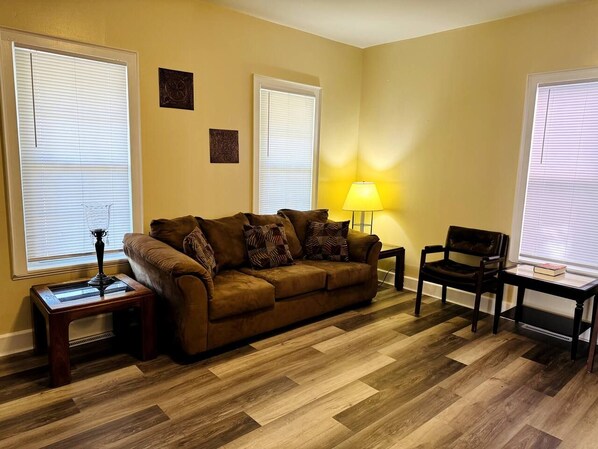 A living room with a brown sofa, two side tables, a lamp, and a chair. - Delightful 4-bedroom house with AC in peaceful Kenosha (Kenosha)