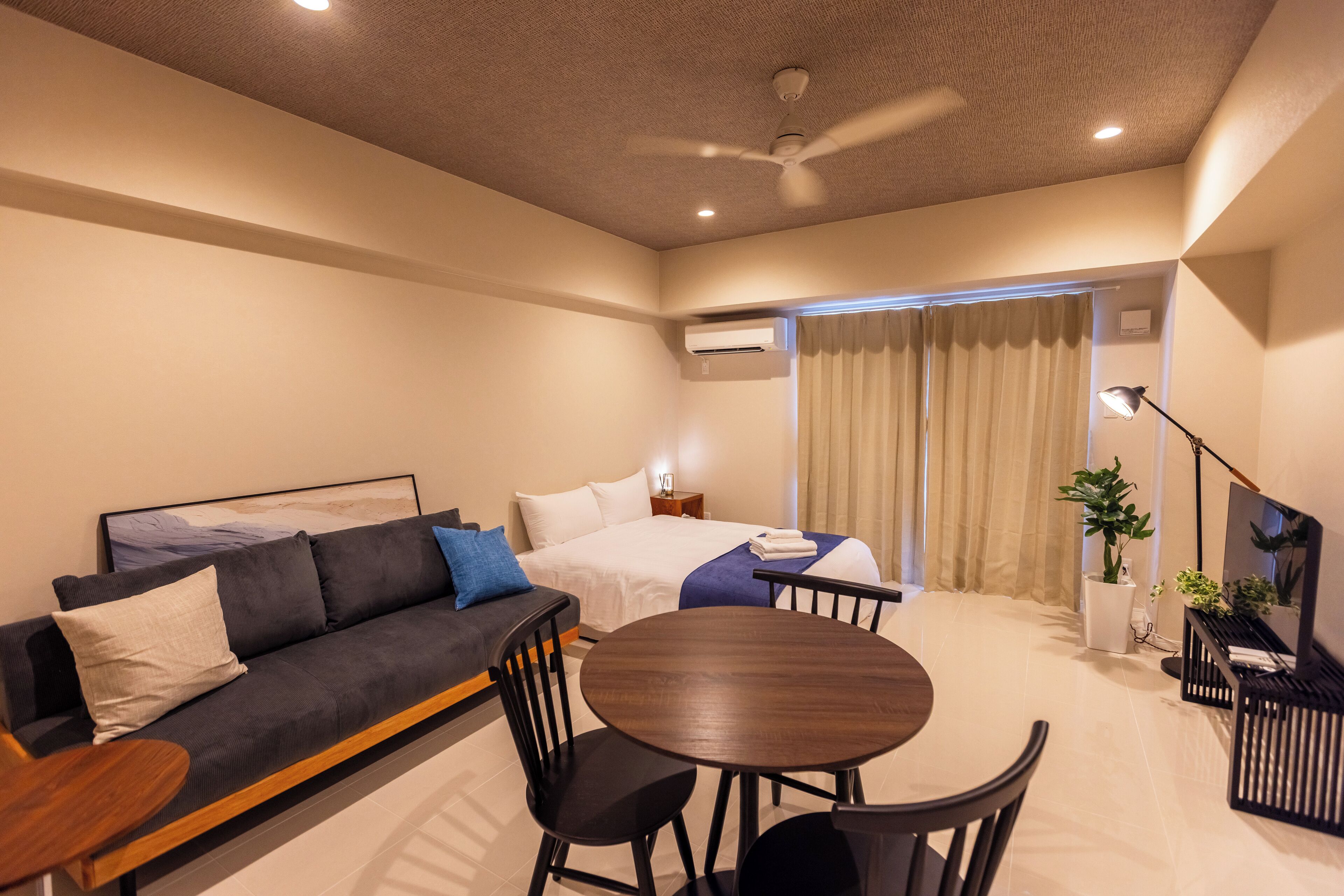 Una habitación de hotel moderna con sofá, una mesa de comedor redonda y un ventilador de techo.