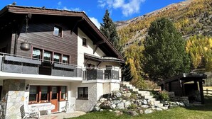 Un chalet de dos pisos con balcón, cimientos de piedra y vistas a un paisaje montañoso.