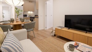A modern living room with a flat-screen TV, a dining area with a wooden table and chairs, and a kitchen in the background. - Apartment + Office in Delicias (Madrid)