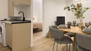 A compact kitchen with a washing machine, a dining area with houndstooth chairs, a table with plates and glasses, and a large potted plant. - Apartment + Office in Delicias (Madrid)