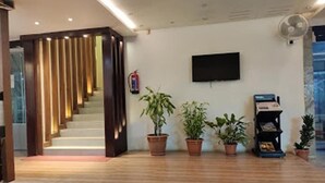 Un hall d’hôtel avec un escalier en bois, un téléviseur à écran plat fixé au mur et plusieurs plantes en pot.