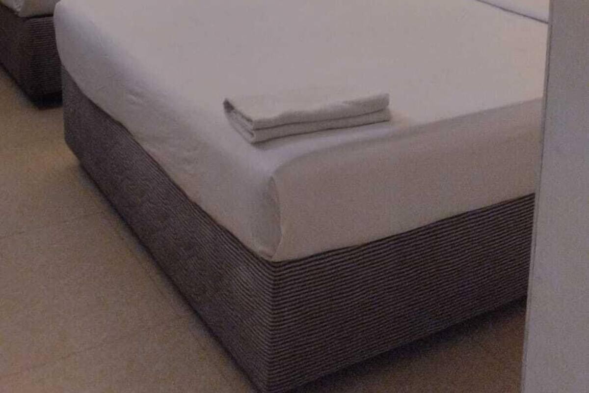 Habitación de hotel con dos camas, cada una con cabecera y almohadas, y un ventanal con cortinas.