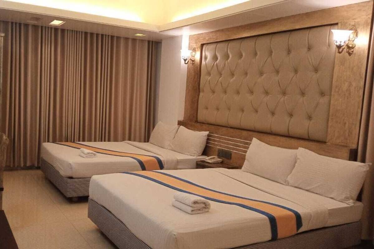 Una habitación de hotel con dos camas, cabecero de madera, un escritorio y una cortina.