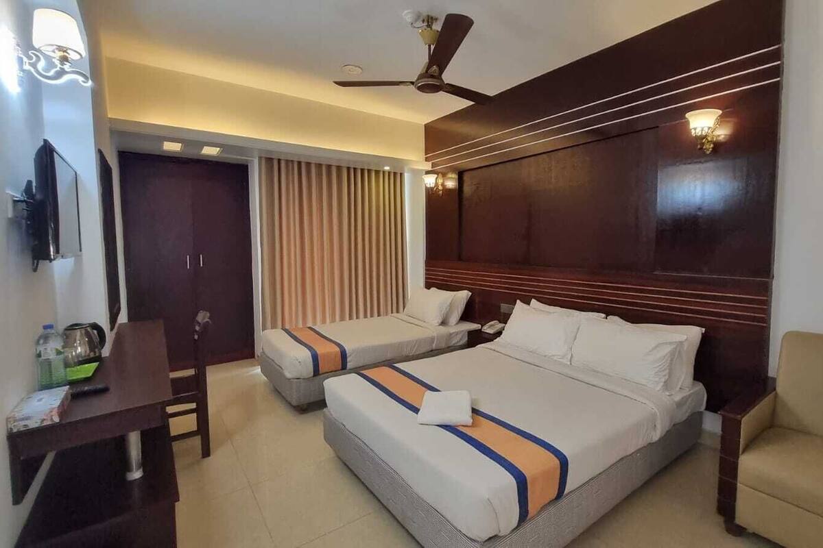 Habitación de hotel con dos camas, un escritorio, una silla, ventilador de techo y ventana con cortinas.