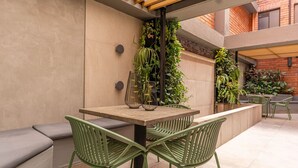 A patio area with a wooden table and green chairs, surrounded by plants and a brick wall. - 1BR-1AC Stylish Studio near Provenza&Parque Lleras (Medellín)