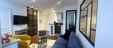 Un salon moderne avec un canapé, un fauteuil et un téléviseur fixé au mur.