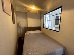 A narrow hotel room with a bed, a large window, a floor lamp, and a wall-mounted light fixture. - Le Cannet Apartmment for 4 Guests (Tanneron)