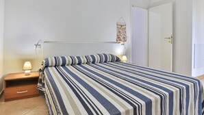 A bedroom with a striped bedspread, bedside lamps, a nightstand, a wall-mounted light fixture, and a door. - Vanna, in Marina di Campo, close to the pedestrian area and to the beach, far from the noise of the (Campo nell'Elba)