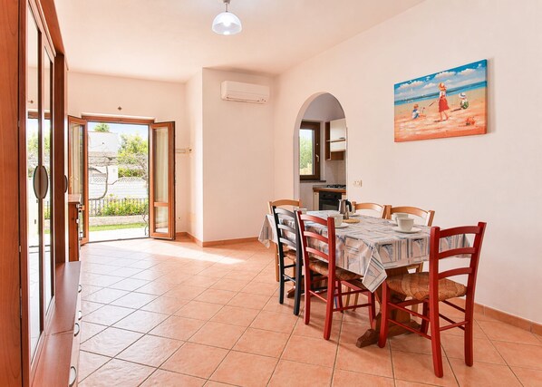 A dining area with a table set for four, a kitchen in the background, and a door leading to a balcony. - Vanna, in Marina di Campo, close to the pedestrian area and to the beach, far from the noise of the (Campo nell'Elba)