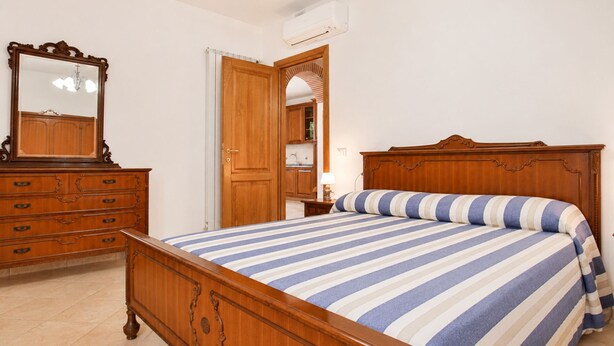 Ein Schlafzimmer mit einem hölzernen Bett, einem Schminktisch, einem Spiegel und einer geöffneten Tür zu einem Badezimmer.