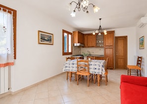 A kitchen with wooden cabinets, a dining table with chairs, a chandelier, and a red sofa. - Three-room apartment Angela, in a quiet area 5 minutes from Marina di Campo, with furnished outdoor (Campo nell'Elba)
