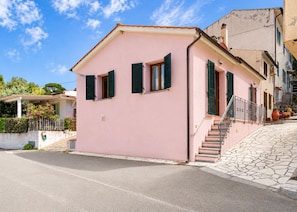A pink building with a small staircase leading to the entrance, a paved driveway, and a clear sky. - Three-room apartment Angela, in a quiet area 5 minutes from Marina di Campo, with furnished outdoor (Campo nell'Elba)