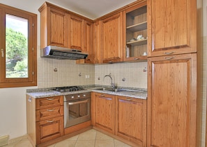 A kitchen with wooden cabinets, a gas stove, stainless steel appliances, and a window with a view of trees. - Three-room apartment Angela, in a quiet area 5 minutes from Marina di Campo, with furnished outdoor (Campo nell'Elba)