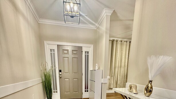 A hallway with wooden flooring, a white door, a white console table with a vase, and a ceiling light fixture.