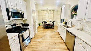 A modern kitchen with white cabinetry, a microwave, stove, and a dining area with a table and chairs.